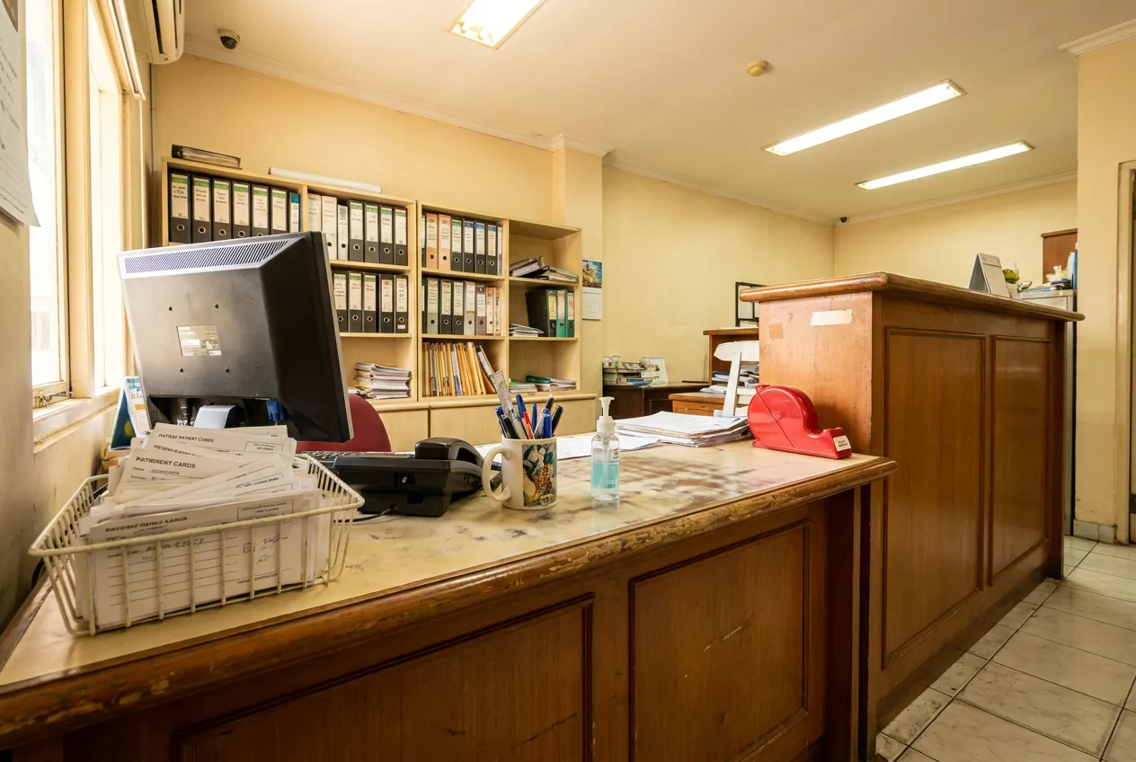 Meja front office Klinik Gigi Aurelia dengan monitor, telepon, rak berkas, dan wadah kartu pasien.